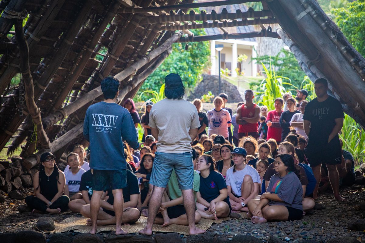 Kānewai workers Kamahaʻo (left) and Kaiona (right) teach their group of volunteers about the moʻolelo, story, of Kānewai. They discuss Hawaiian akuas, gods, and answer questions from the volunteers inside the Hale Waʻa, house of the canoe.