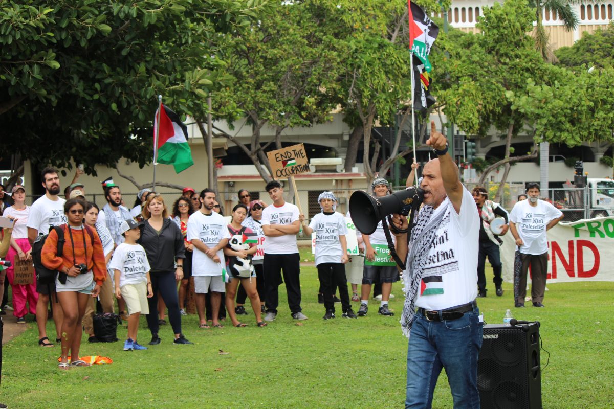 Hakim Ouansafi, the Board Chairman of the Muslim Association of Hawaii, delivers a brief speech to the attendees just moments before the march kicks off.

Audio Description: A man is standing in front of a group of attendees. He is shouting through a megaphone while pointing upward. The watchers are looking at him with some holding signs. They are a lot of protestors in the park, looking at Ouansafi.