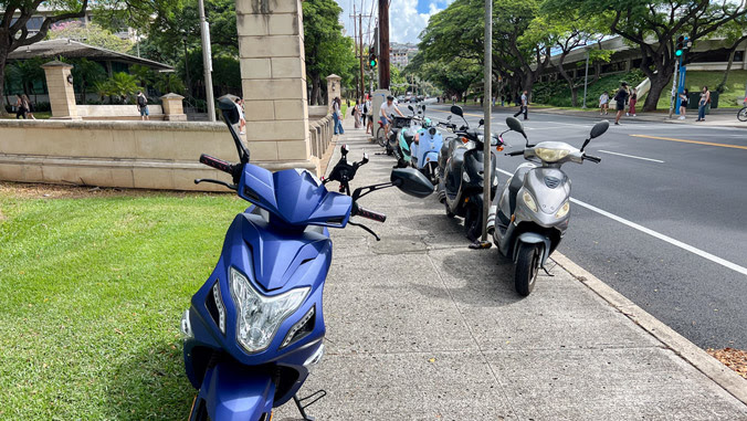 A photo of Mopeds parked illegally on the sidewalk of UH Mānoa's campus. 