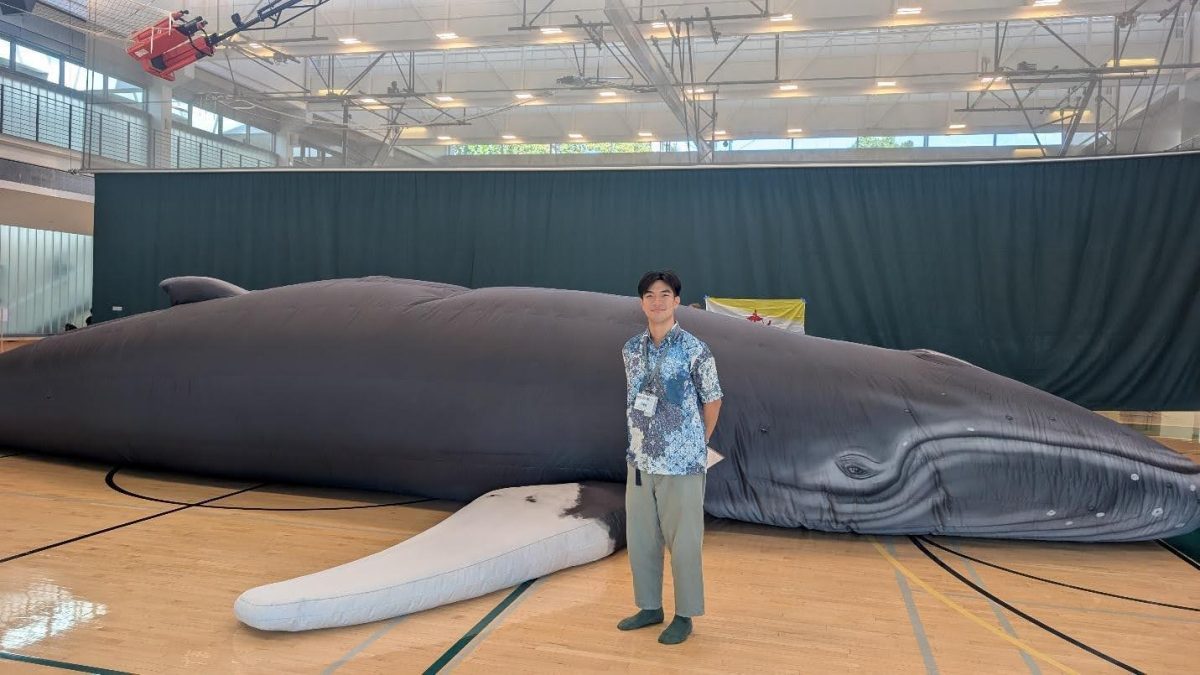 Nopasin Chaiparichat standing in front of the humpback whale model in the Warrior Recreation Center