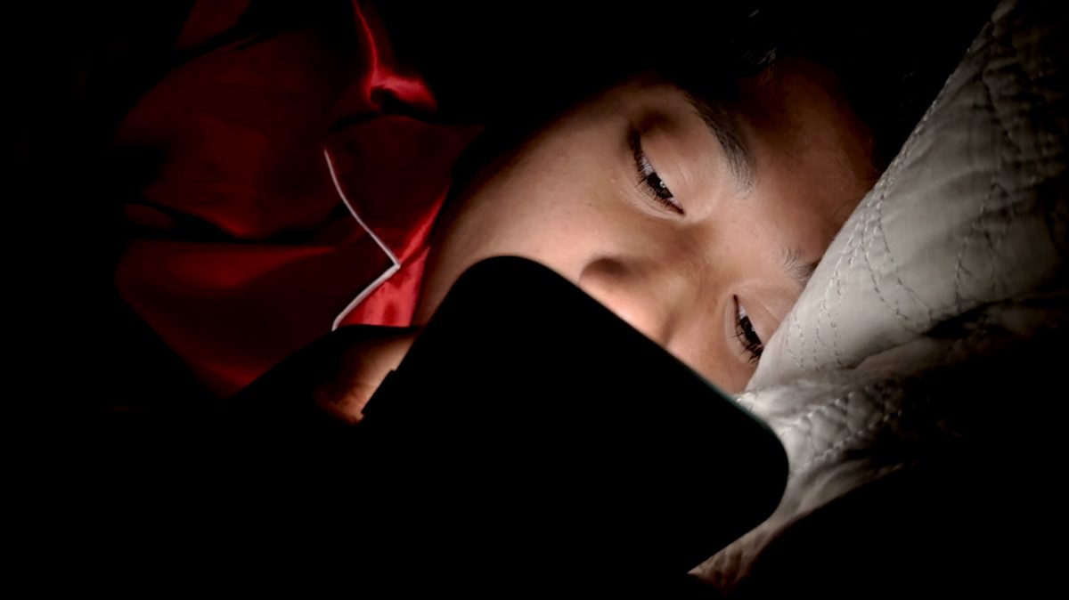 A student scrolling through their phone in bed.